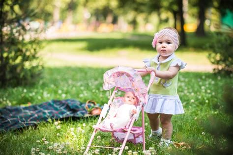 Bambina che spinge un passeggino giocattolo in un parco con la sua bambola
