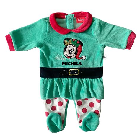 Bebè vestito con una tutina natalizia che gioca con decorazioni festive in un ambiente accogliente