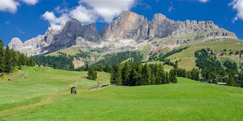Panorama della Val di Fassa con pascoli verdi e vette dolomitiche sullo sfondo