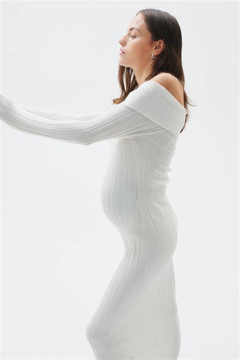 Donna incinta in abito bianco a spalle scoperte in un campo di fiori selvatici