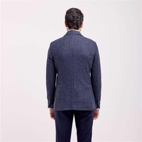 Un blazer sartoriale da uomo esposto in un atelier luminoso con tessuti naturali in primo piano