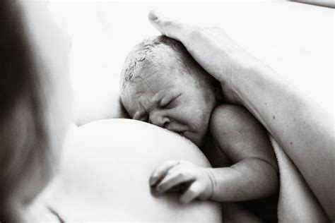 Una madre che tiene in braccio il proprio neonato appena nato in sala parto, circondata da un'atmosfera serena e di supporto.