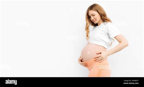 Mamma incinta che tocca il pancione sorridendo, circondata da piccoli capi di abbigliamento per neonati