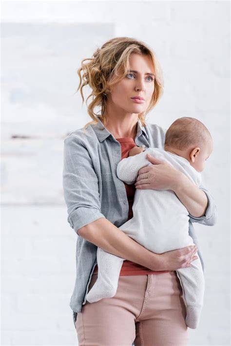 Madre moderna stanca con smartphone e bambino in braccio