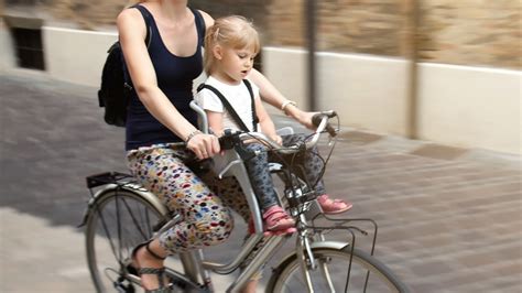 genitore che pedala con bambino su seggiolino anteriore in città