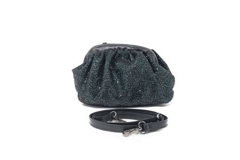 dettaglio di una pochette gioiello nera con borchie oro posata su un tavolo in seta