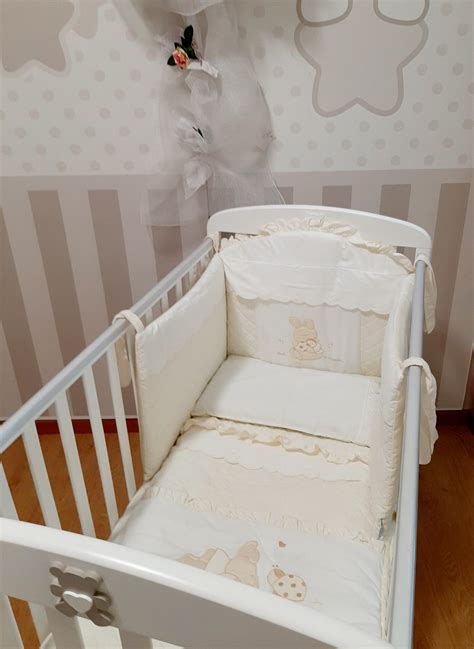 Un lettino per neonato arredato con un set paracolpi dai colori tenui e tessuti morbidi