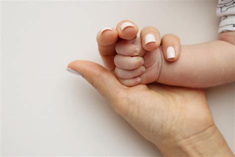 Mano di madre che tiene la mano di un neonato in un ambiente sereno ma con un'ombra sottile