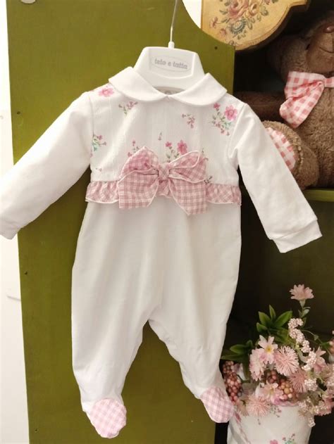 Una tutina neonata in cotone delicato poggiata su un set tessile bianco con luce naturale