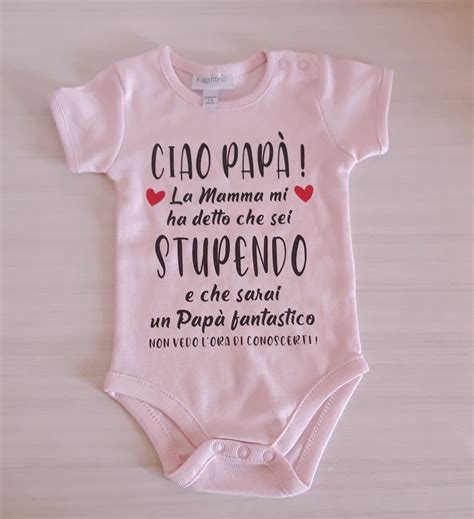 Un neonato che indossa un body personalizzato con una scritta affettuosa rivolta al papà, in un ambiente domestico luminoso.