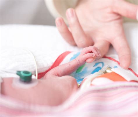 Manine di neonato prematuro che stringono il dito di un adulto