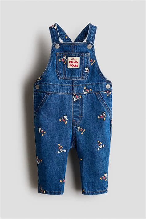 Un dettaglio ravvicinato di una salopette in denim con stampa a cuori e una selezione di accessori abbinati su un tavolo di legno.