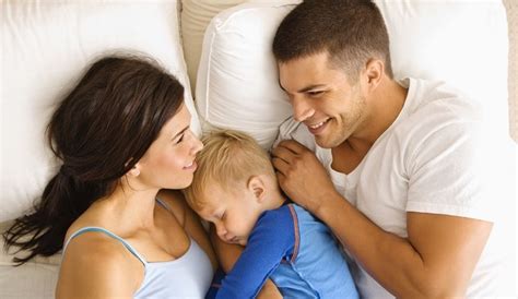 Famiglia che dorme insieme nel lettone, con il neonato sereno tra i genitori