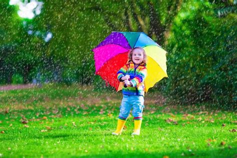 bambina che gioca felicemente sotto la pioggia indossando stivali colorati