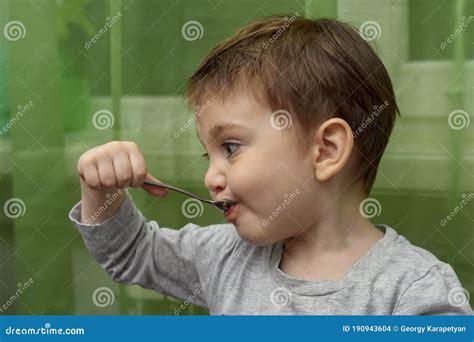 Bambino che mangia con un cucchiaino, con espressione curiosa