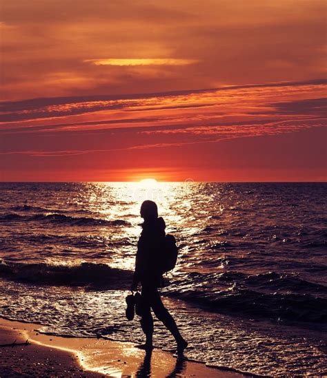 Donna incinta che cammina sulla spiaggia al tramonto