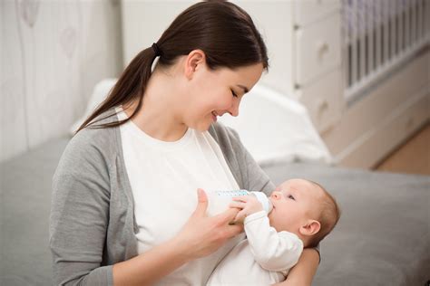 Mamma che dà il biberon al bambino con attenzione e contatto visivo