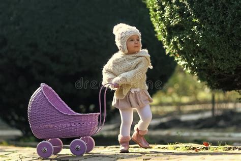 Una bambina che passeggia con una carrozzina per bambole in un parco fiorito