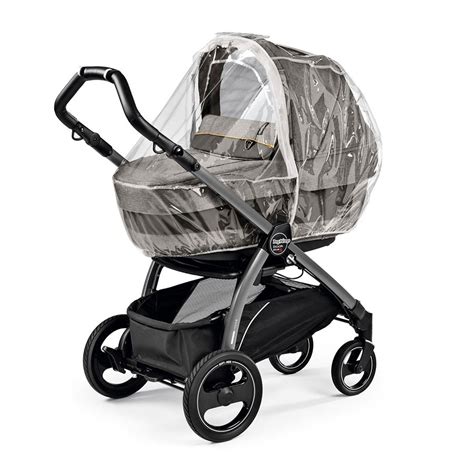 Un bambino felice riparato in un passeggino Peg Perego protetto da un parapioggia trasparente durante una giornata di pioggia leggera.
