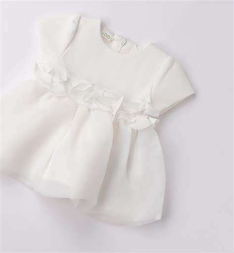 un elegante abito da battesimo per neonato appeso su un fondo bianco minimalista