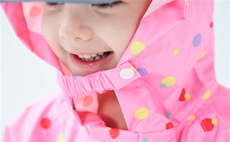 Bambina felice con giacca impermeabile colorata sotto la pioggia