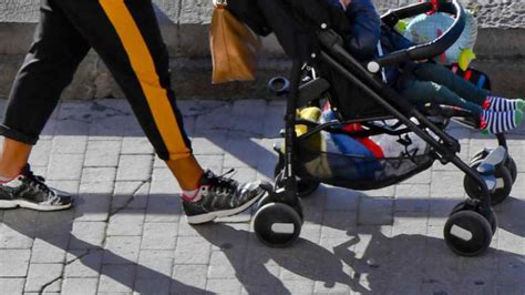 Genitore che spinge un passeggino leggero in una strada cittadina trafficata