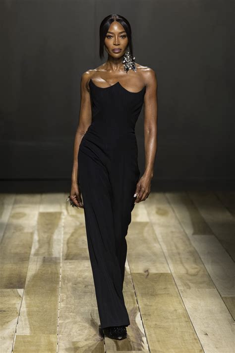 Modella che sfila in passerella indossando un catsuit nero aderente in jersey lucido, stile iconico lanciato da Anthony Vaccarello