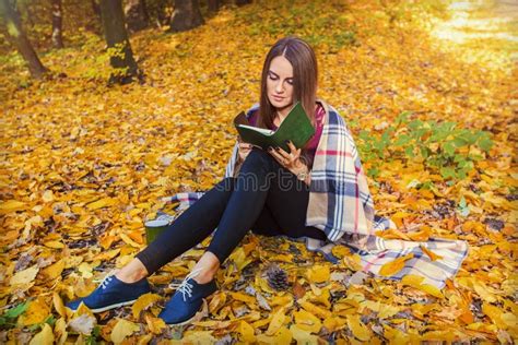 Una giovane donna con un libro in mano, seduta in una foresta autunnale