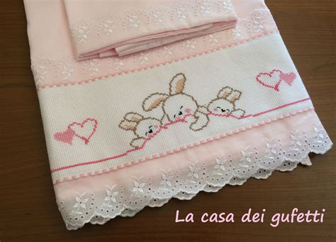 immagine di un corredo per neonato elegantemente ricamato a punto croce su un lenzuolino in cotone bianco