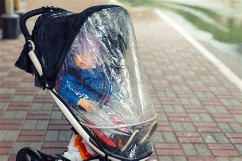 Bambino felice in passeggino sotto la pioggia con protezione trasparente