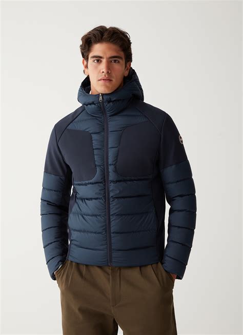 Un bambino neonato che indossa un soffice piumino Colmar blu in un contesto invernale urbano