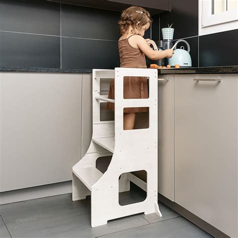 Bambina sulla torre di apprendimento che osserva gli adulti in cucina