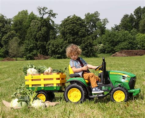 Un bambino che guida un trattore elettrico Peg Perego John Deere Ground Force con rimorchio