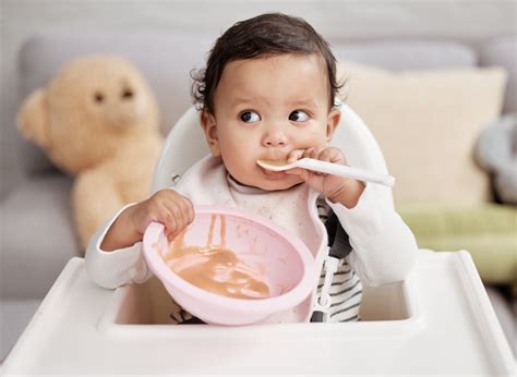 Image of a baby happily eating from a spoon, with a bowl of baby food