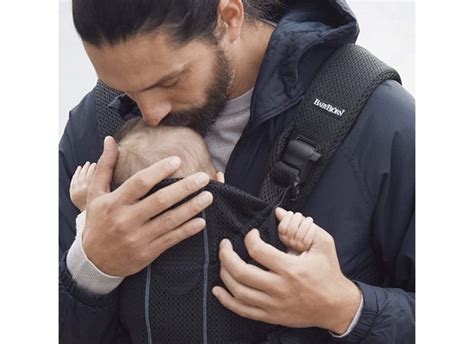 Bambino di pochi mesi rivolto verso il genitore in un marsupio