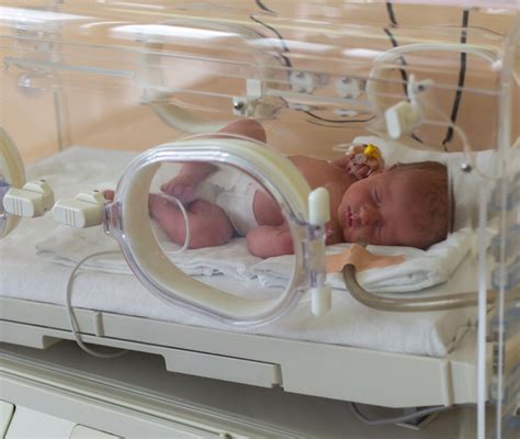 Bambino prematuro in incubatrice con un piccolo cappellino