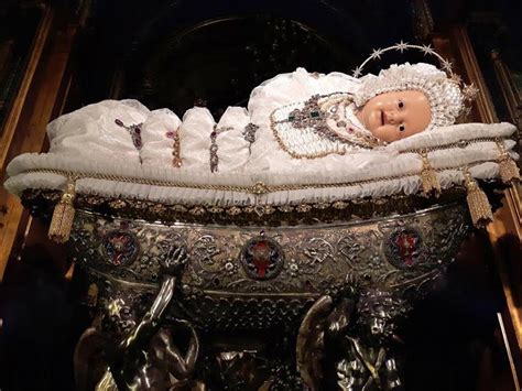 Una suggestiva immagine di Maria Bambina custodita in una culla, protetta da una campana di vetro e circondata da decorazioni floreali.