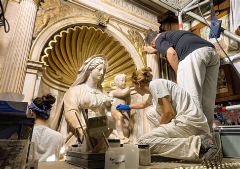 Un artigiano che lavora al restauro di una statuetta antica di Maria Bambina, evidenziando la delicatezza delle stoffe e dei materiali utilizzati.