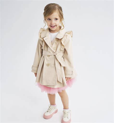 Bambina con trench beige classico in un parco autunnale