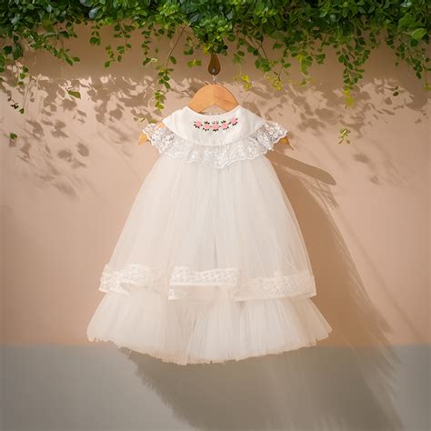 Close-up of a baby's delicate hand touching a soft, embroidered baptism gown