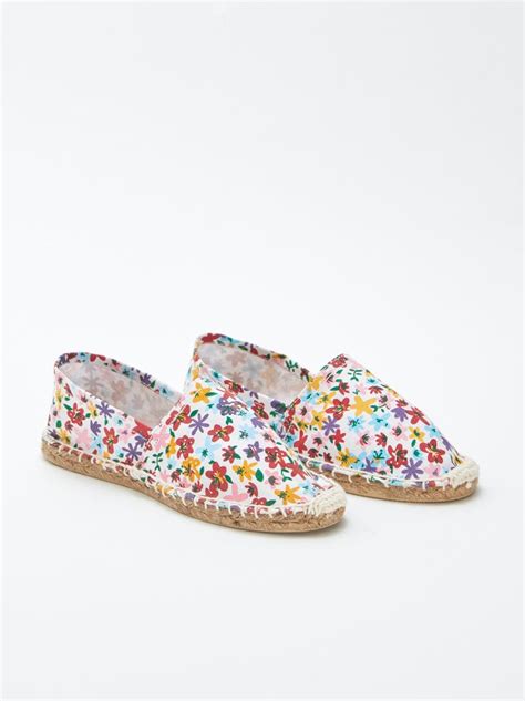 Donna con tutina a fiori e espadrillas, con una pochette in rafia