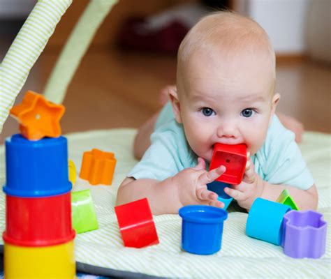 Bambino di 6 mesi che gioca con giocattoli morbidi, indossando un pigiamino Prénatal